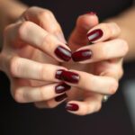 Klasyczne paznokcie żelowe bordowe w jednolitym kolorze na dłoniach kobiety